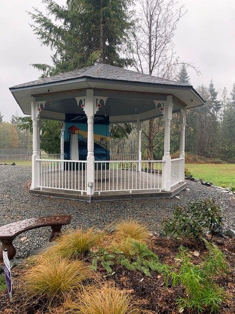 The white gazebo beside the branch, with a garden bed in front.